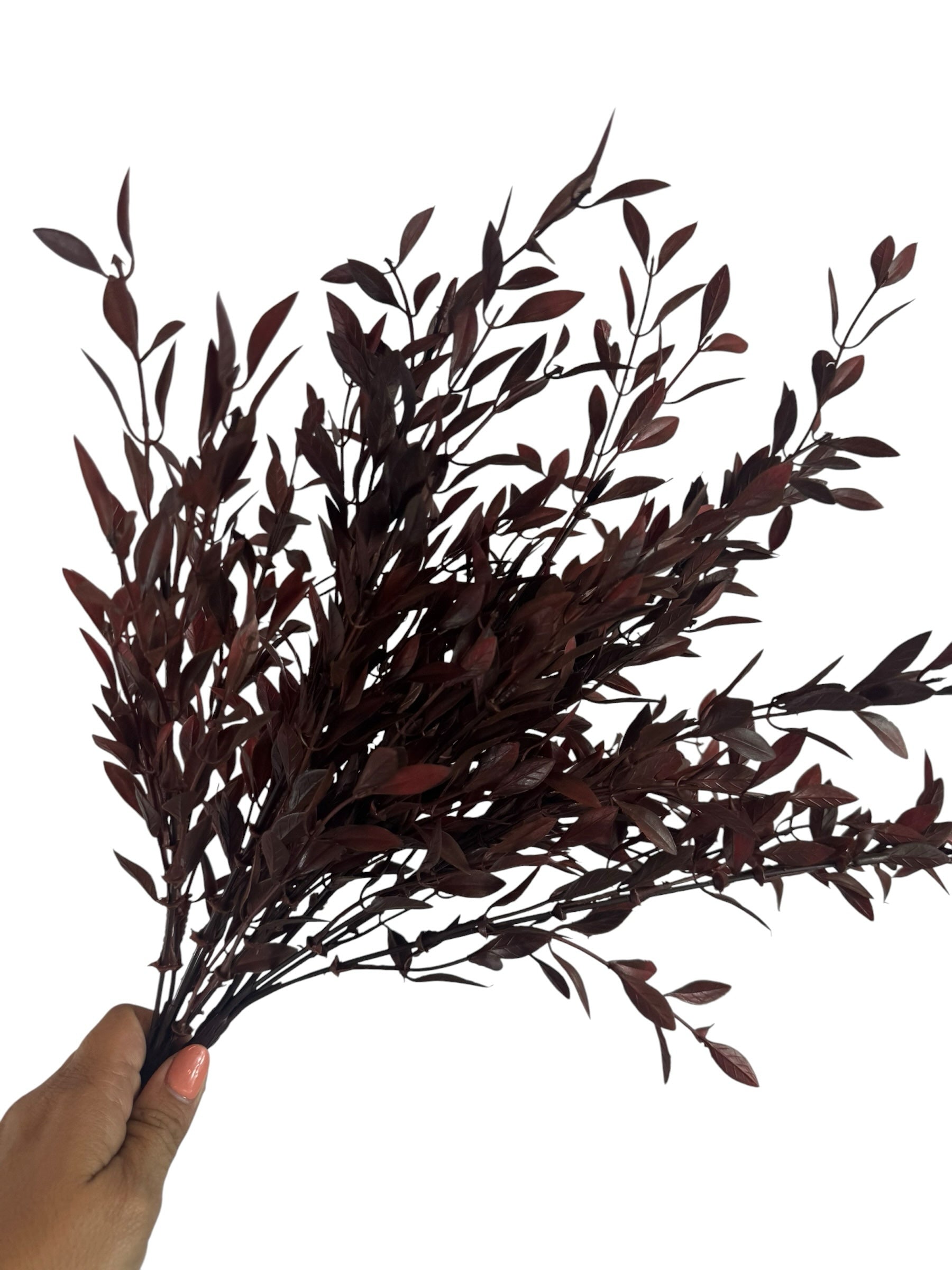 Artificial Bloom deep burgundy faux leafy branch stem with realistic foliage held in a hand against a white background