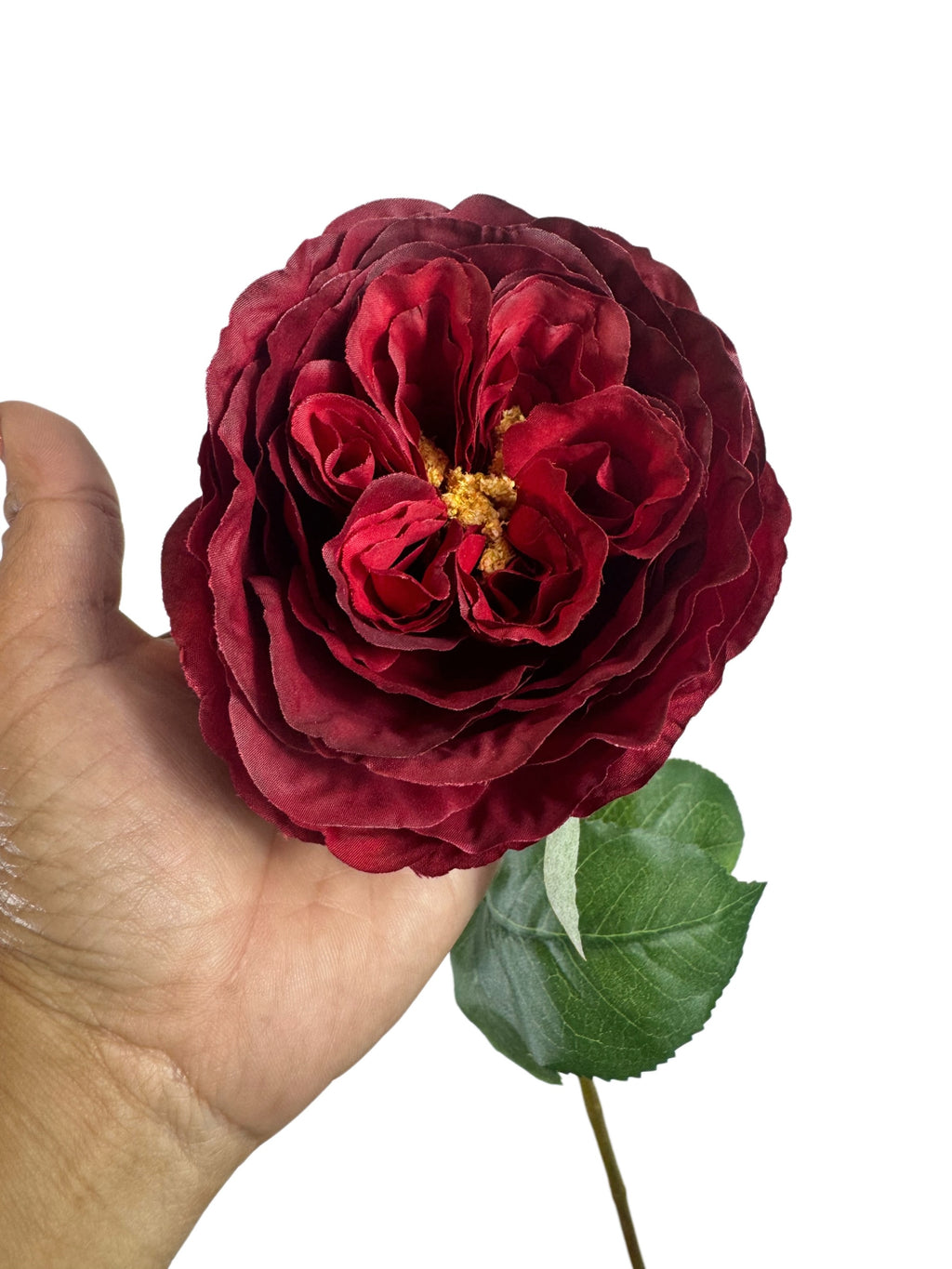 Artificial Bloom deep red faux rose stem with velvety petals and realistic green foliage held in a hand