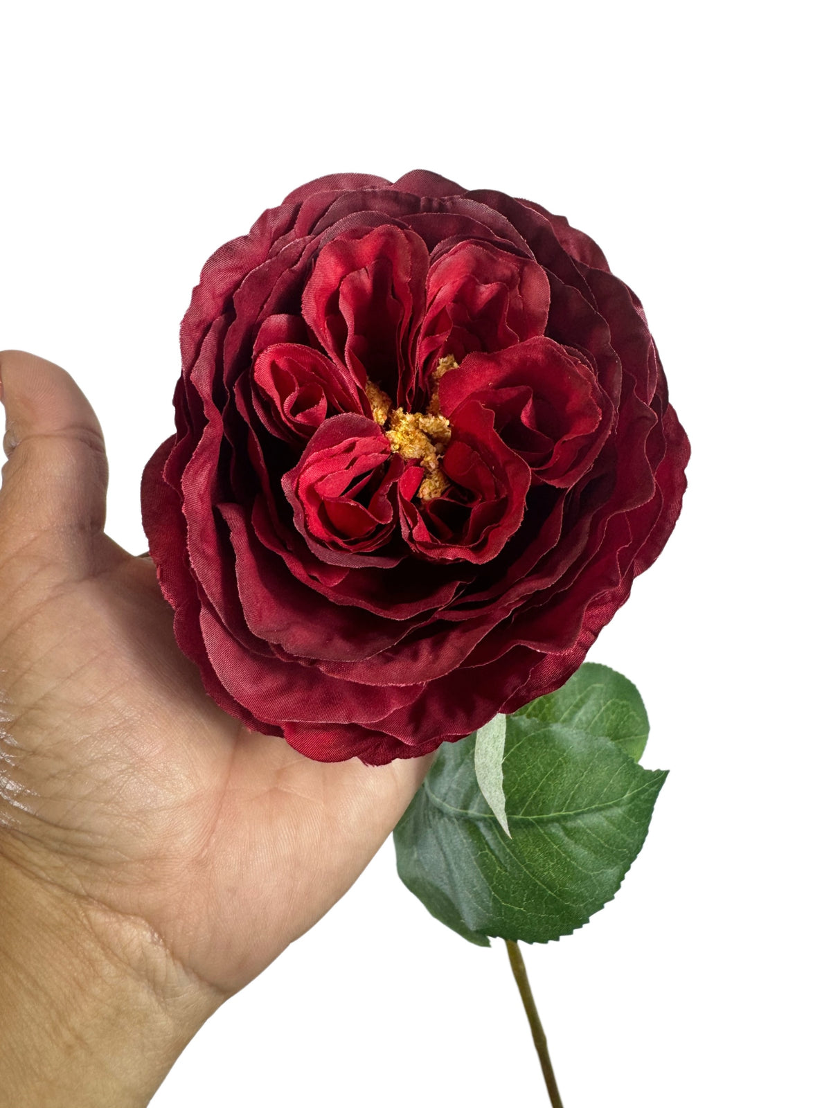 Artificial Bloom deep red faux rose stem with velvety petals and realistic green foliage held in a hand