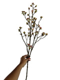 Artificial Bloom decorative flowering branch with textured brown bark, soft fuchsia                                                                                                                                                                                                                                                             buds, and green leaves held by a hand.