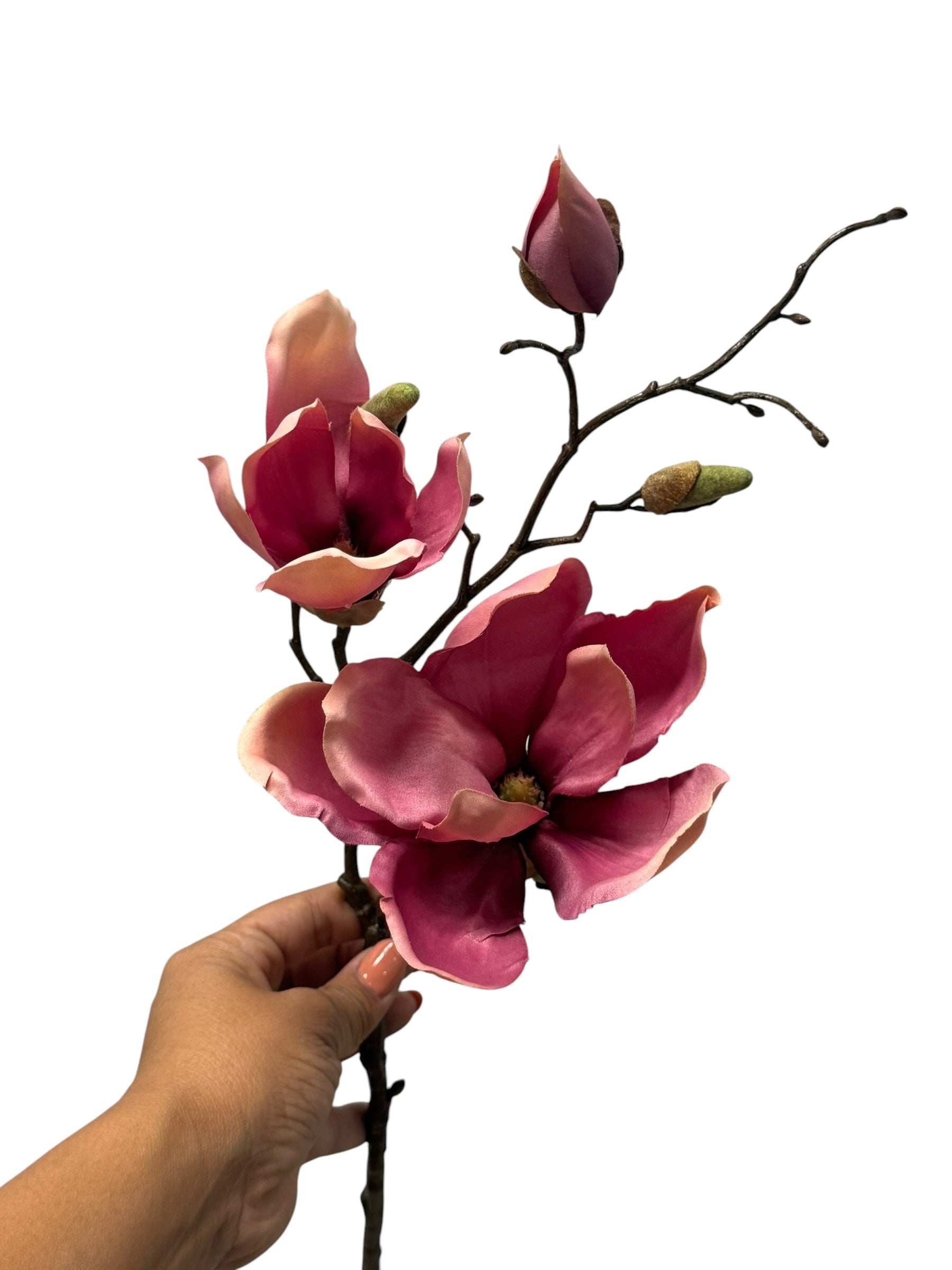 Artificial Bloom magenta and pink velvet magnolia floral stem held by a hand against a white background