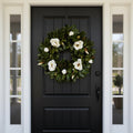 Artificial Bloom magnolia leaf and white blossom wreath hanging on a classic black front door.