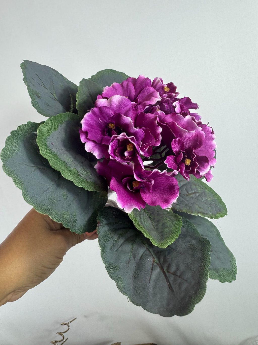 Artificial Bloom artificial African Violet with deep purple flowers and textured green leaves held in a hand