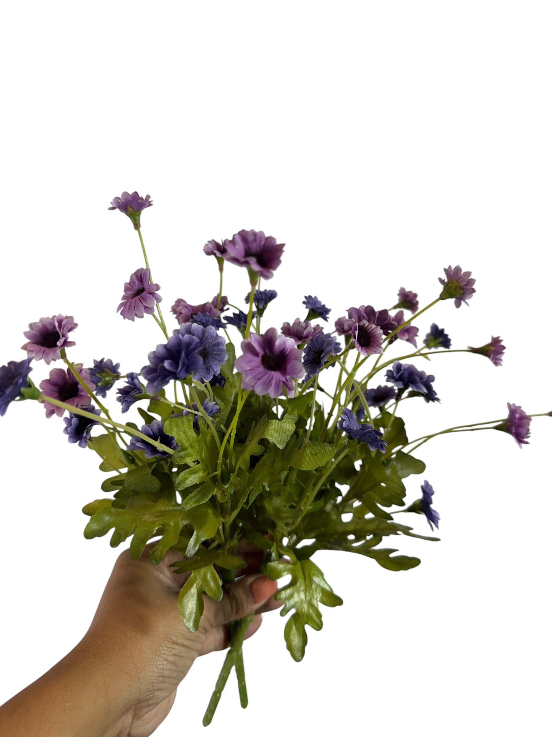 Artificial Bloom purple and lavender fabric daisy bouquet with green foliage held in a hand against white background