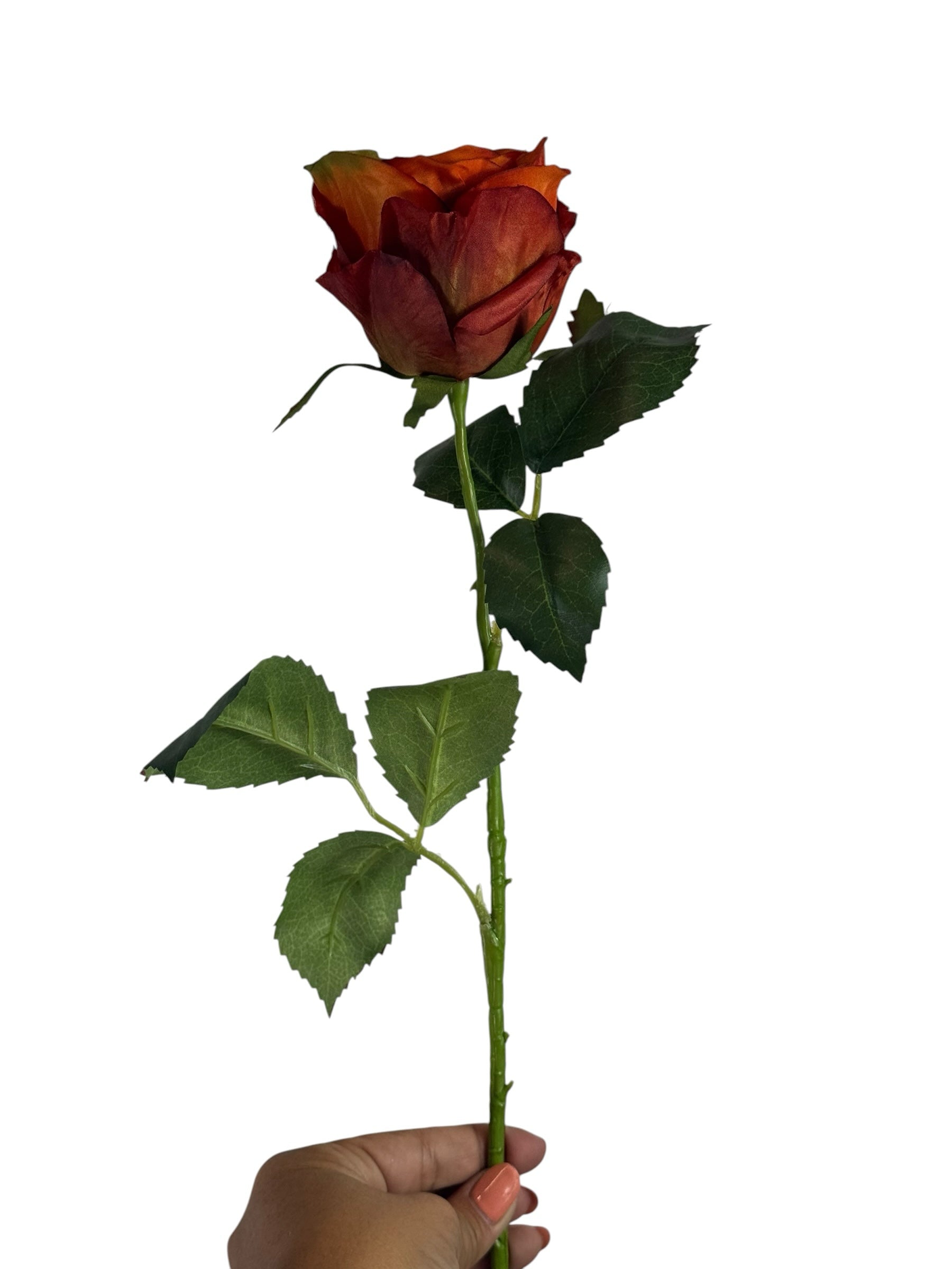 Artificial Bloom rust-orange silk rose stem with realistic green leaves held by a hand against a white background