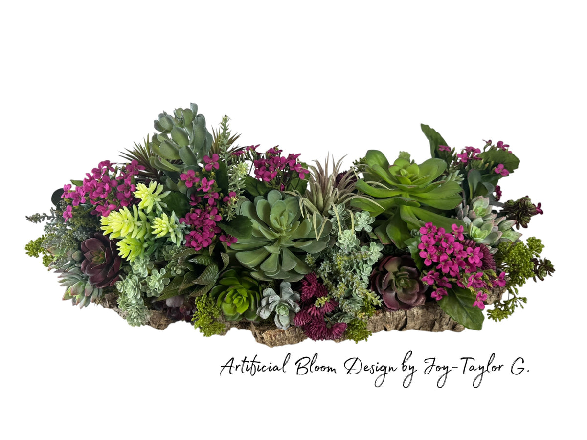 Artificial Bloom succulent centerpiece with green and purple faux plants and magenta flowers on a rustic cork bark base.