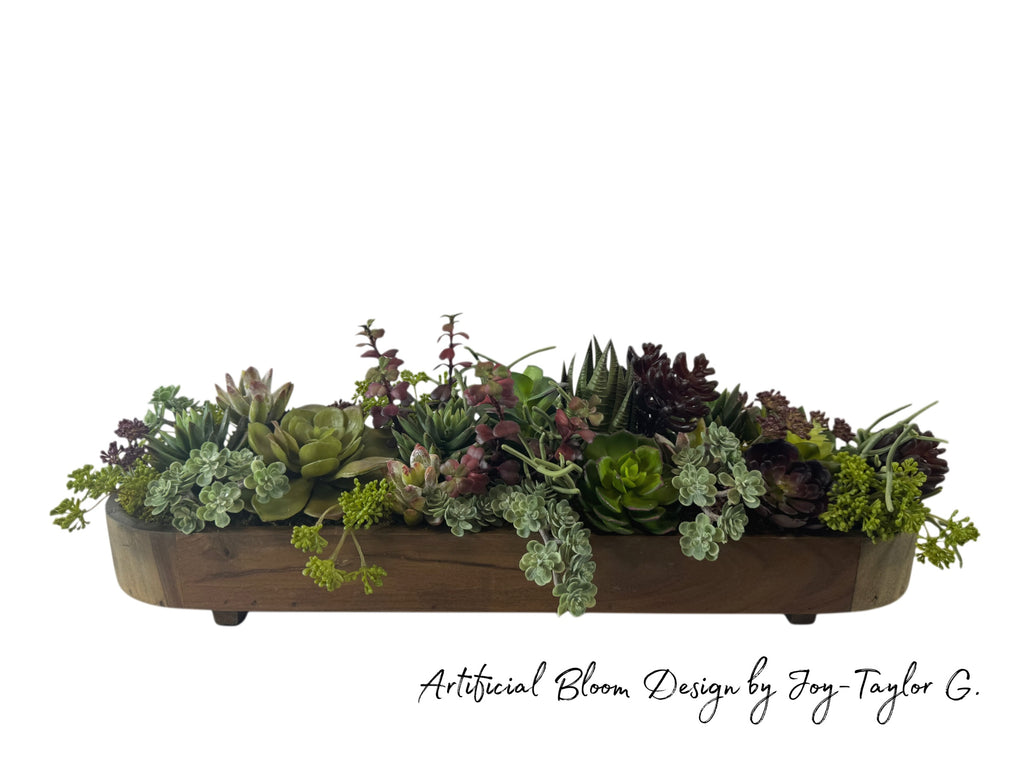 Artificial Bloom succulent arrangement featuring green and burgundy faux plants in a rustic wooden trough centerpiece.